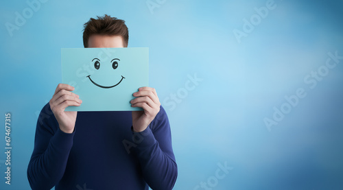 person covers his face with cardboard, with a drawing of a smiling face