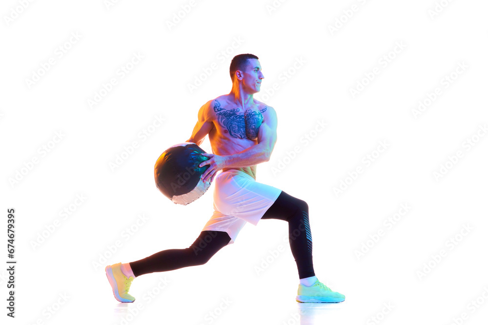 Muscular young man training shirtless with fitness ball, moving forward against white studio background in neon light. Concept of sport, active and healthy lifestyle, body, fitness. Copy space for ad Muscular young man training shirtless with fitness ball, moving forward against white studio background in neon light. Concept of sport, active and healthy lifestyle, body, fitness. Copy space for ad