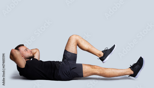 Concentrated handsome strong young caucasian guy with beard in sportswear make exercises for legs and abs