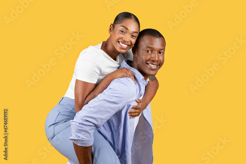 Playful piggyback couple smiling against yellow background