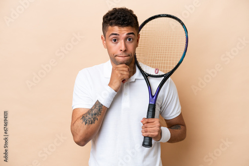 Young brazilian handsome man playing tennis isolated on beige background having doubts and thinking © luismolinero