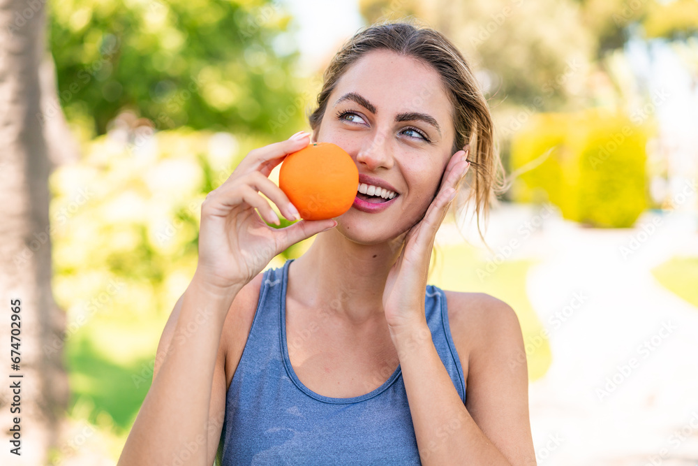 Young blonde woman at outdoors holding an orange Young blonde woman at outdoors holding an orange