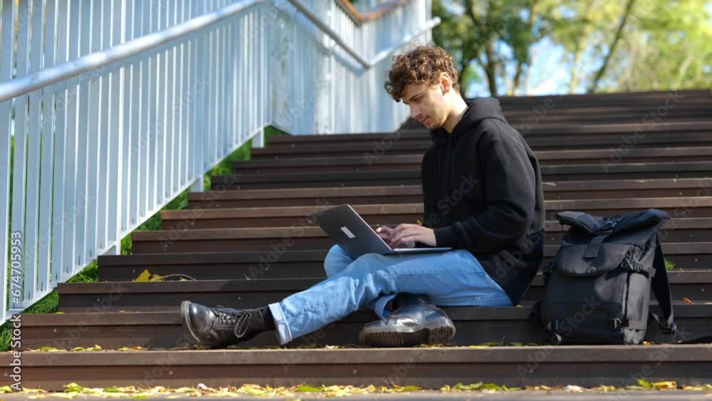 Young man sitting on the staircase in the city park while using laptop and typing. Autumn season. Education, working concept. Real time concept. Young man sitting on the staircase in the city park while using laptop and typing. Autumn season. Education, working concept. Real time concept.