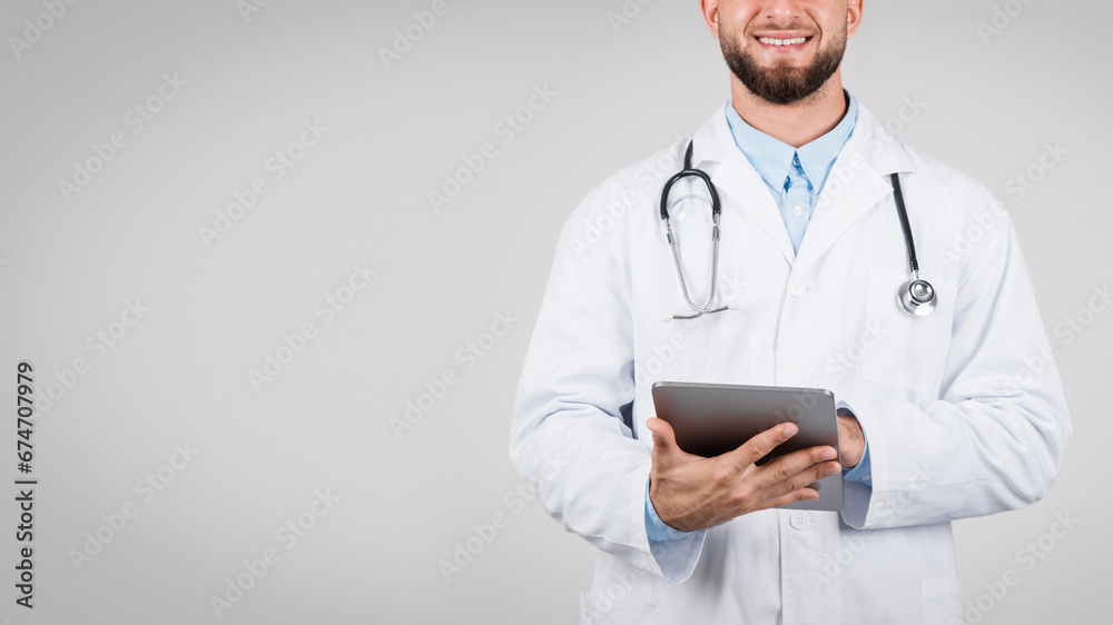 Smiling man doctor holding a digital tablet, grey background, panorama with free space Smiling man doctor holding a digital tablet, grey background, panorama with free space