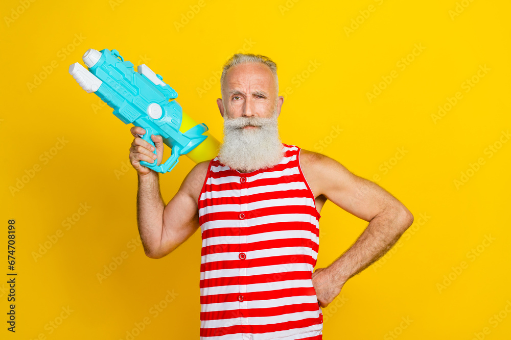 Photo of serious brutal pensioner man wear striped overall prepare for swimming pool water guns battle isolated on yellow color background Photo of serious brutal pensioner man wear striped overall prepare for swimming pool water guns battle isolated on yellow color background