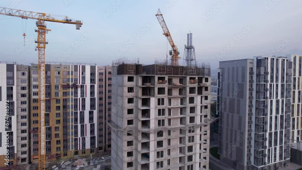Construction of tall houses near the road. The city of Almaty. New multi-storey buildings are being built. Builders, crane, machines are working. Aerial view of houses and roads from the drone. Construction of tall houses near the road. The city of Almaty. New multi-storey buildings are being built. Builders, crane, machines are working. Aerial view of houses and roads from the drone.
