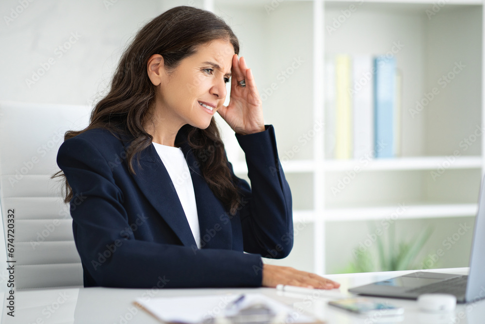 Sad middle aged woman working at office, suffering from headache Sad middle aged woman working at office, suffering from headache