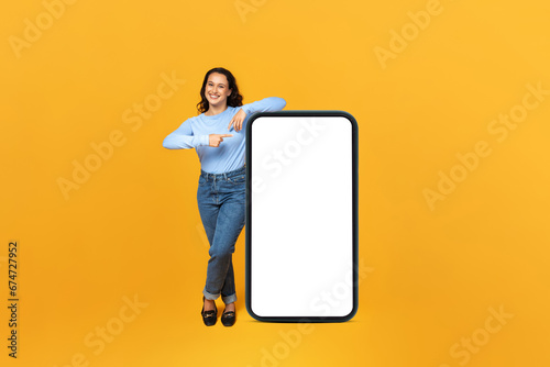 Cheerful millennial lady showing huge phone with blank screen