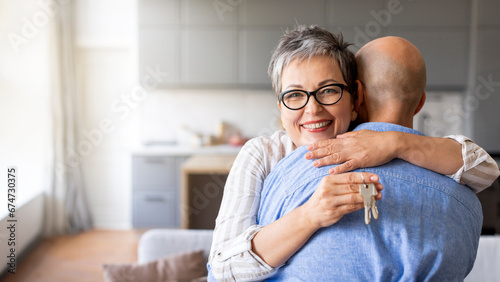 Happy senior woman hugging husband and holding home keys in hand photo