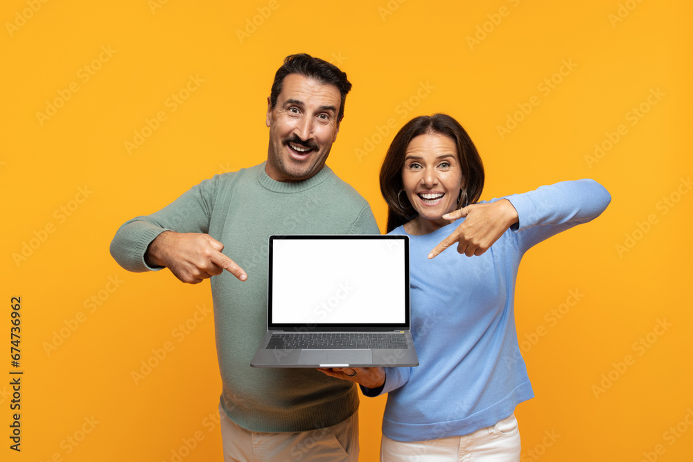 Glad excited funny senior european man and lady point finger at laptop, with empty screen Glad excited funny senior european man and lady point finger at laptop, with empty screen