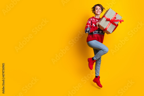 Full body photo of satisfied cute woman with stylish hair wear sweater hold present box jumping isolated on yellow color background