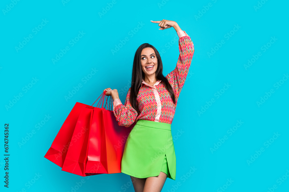 Photo portrait of attractive young woman shopping bags point empty space wear trendy green skirt isolated on cyan color background Photo portrait of attractive young woman shopping bags point empty space wear trendy green skirt isolated on cyan color background