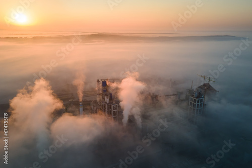 Aerial view of cement factory with high concrete plant structure and tower crane at industrial production site on foggy morning. Manufacture and global industry concept © bilanol
