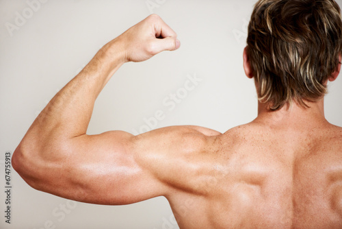 Back, arm and a man flexing his bicep in studio isolated on a gray background for health, fitness or wellness. Exercise, training and strong with the body of a shirtless model from behind for power photo