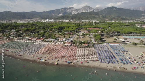 Aerial view of the beach in Massa with people sunbathing and long lines with umbrellas, Italy.