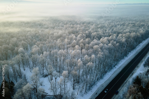 Aerial view of winter landscape with snow covered woods and black asphalt forest road on cold wintry day