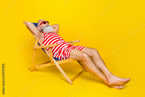 Full length photo of relaxing funky senior man wear red striped lying deck chair hands behind head empty space isolated yellow color background photo