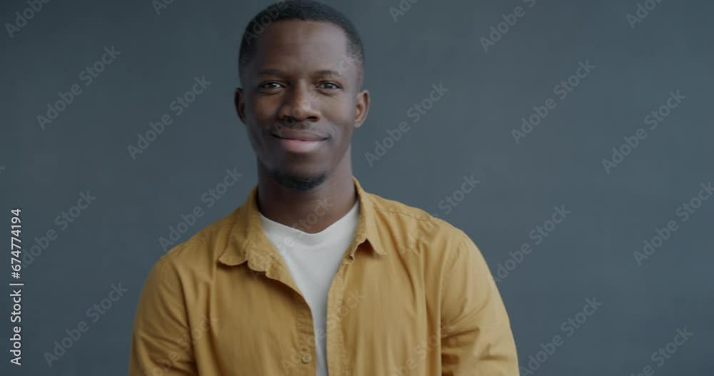 Slow motion portrait of cheerful African American man staring at camera through imaginary binoculars and smiling on grey color background