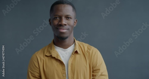 Slow motion portrait of cheerful African American man staring at camera through imaginary binoculars and smiling on grey color background