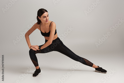 sportswoman in active wear with fitness tracker on wrist doing lunges on grey backdrop  motivation