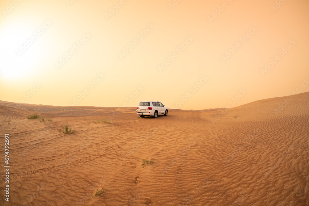 SUV truck parked on a sand dune near Dubai, UAE, sunset sky in the background. Extreme sports, adventure and travel concept. Wide angle shot.