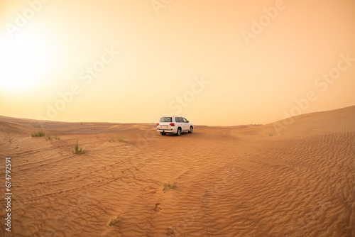 SUV truck parked on a sand dune near Dubai, UAE, sunset sky in the background. Extreme sports, adventure and travel concept. Wide angle shot.