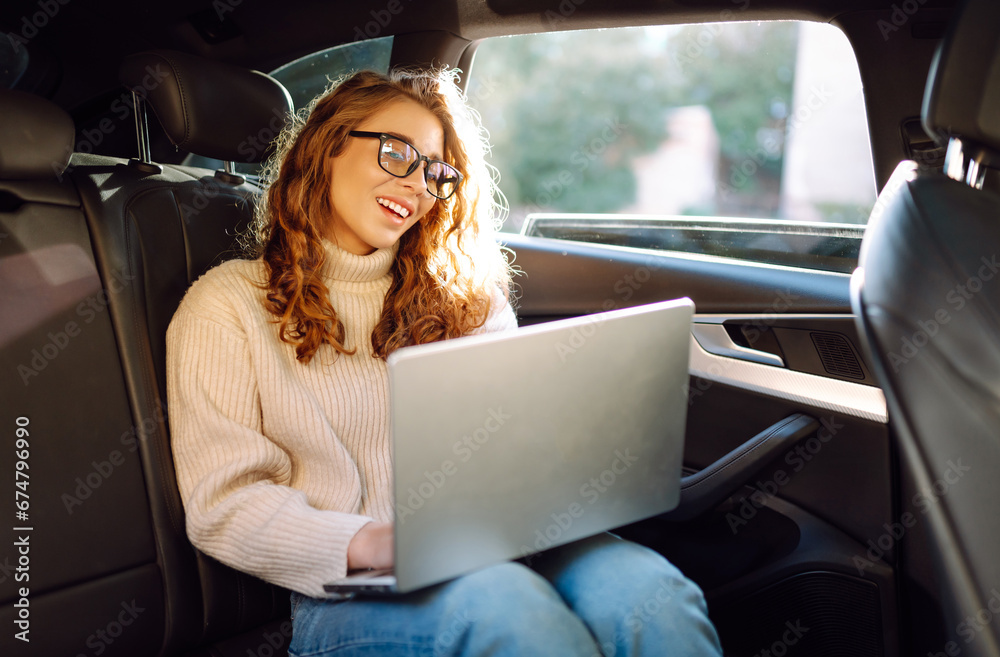 Young woman with a laptop in the back seat of a car. Business woman working on a laptop in a car. Freelance, business concept. Young woman with a laptop in the back seat of a car. Business woman working on a laptop in a car. Freelance, business concept.
