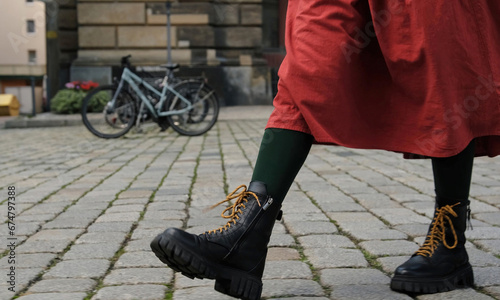Girl In Red Skirt Walks By Historical Part Of European City, Legs Clad In Black Boots