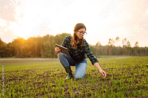 Young female agronomist with a digital tablet in her hands checks young shoots in the field. A female farmer using a modern tablet checks the growth of her crop. Agriculture concept.