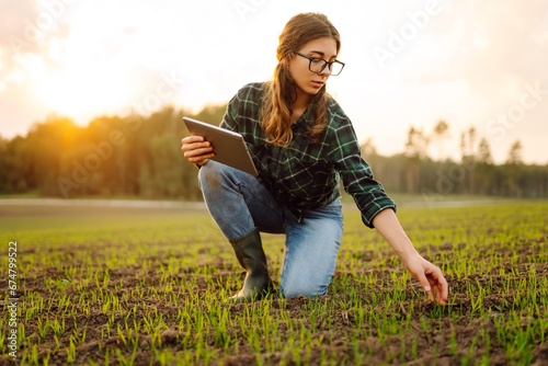 Young female agronomist with a digital tablet in her hands checks young shoots in the field. A female farmer using a modern tablet checks the growth of her crop. Agriculture concept.