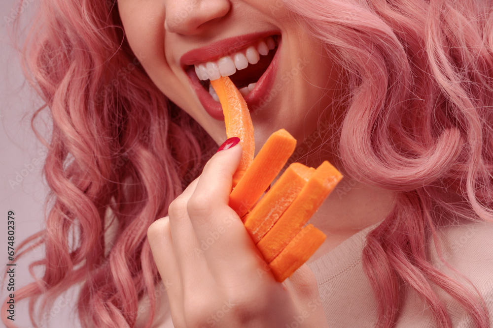 Carrots cut into strips in woman hand. Woman with pink curly hair is eating carrot. Carrots cut into strips in woman hand. Woman with pink curly hair is eating carrot.