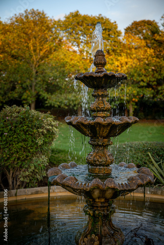 Fountain in a park with the setting sun illuminating the background trees. Portrait view.