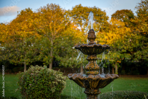 Fountain in a park with the setting sun illuminating the background trees. Landscape view.