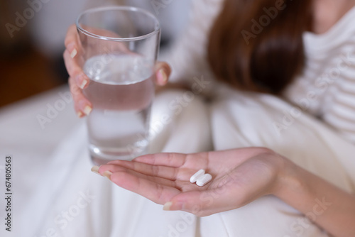 Close-Up on sick asian woman holding medicine and glass of water in her hand