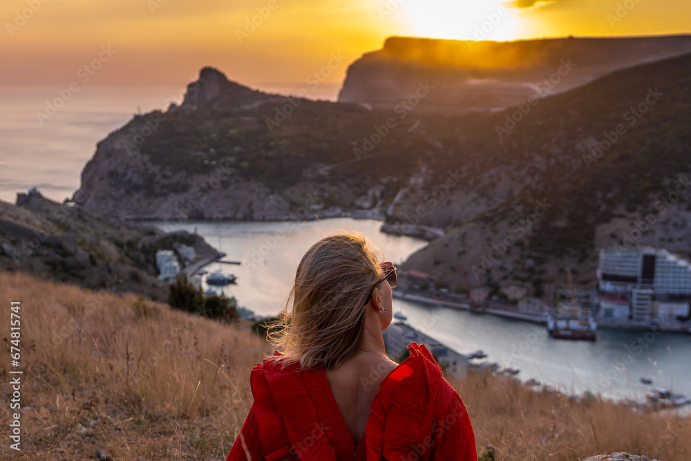 Woman sunset sea mountains. Happy woman siting with her back on the sunset in nature summer posing with mountains on sunset, silhouette. Woman in the mountains red dress, eco friendly, summer landscap