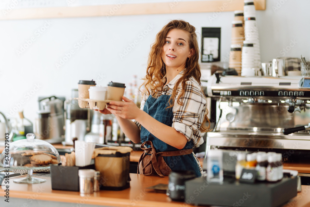 Female barista holding disposable takeaway cups. The young barista owner behind the bar gives out to-go orders. Business concept. Drinks to go. Female barista holding disposable takeaway cups. The young barista owner behind the bar gives out to-go orders. Business concept. Drinks to go.