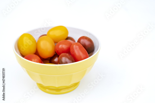Colorful cherry tomatoes in a jellow bowl. Fresh  ripe type of small and round cocktail tomatoes  of red  yellow and orange color. Solanum lycopersicum var. cerasiforme. Isolated  close up  from above
