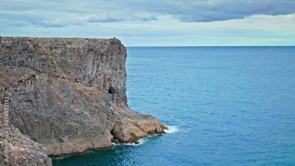 Tourists climbing the mountain rocky formation at Huntsman's Leap in Wales. Stunning panoramic sea views with a cliff gap near Saint Govan's Chapel on the cliffside. Tourists climbing the mountain rocky formation at Huntsman's Leap in Wales. Stunning panoramic sea views with a cliff gap near Saint Govan's Chapel on the cliffside.