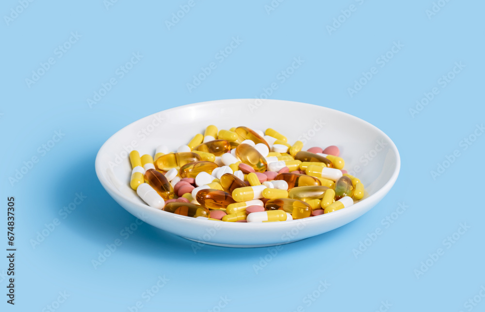 Many colorful pills, omega 3 vitamins and nutrition supplements in white plate on blue background. Medical treatment or weight loss drugs. Diet and healthy lifestyle Many colorful pills, omega 3 vitamins and nutrition supplements in white plate on blue background. Medical treatment or weight loss drugs. Diet and healthy lifestyle