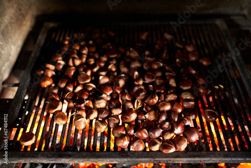 Bunch of fresh chestnuts is baked on coals on a grill grate in an oven