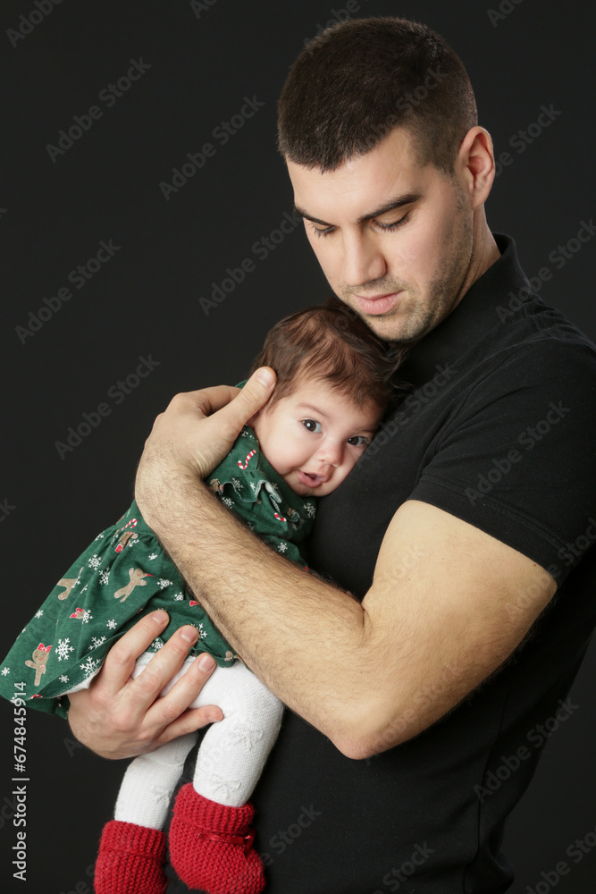 Studio portrait of father holding his little baby girl in green Christmas outfit, winter holiday, family memories, the first Christmas together Studio portrait of father holding his little baby girl in green Christmas outfit, winter holiday, family memories, the first Christmas together