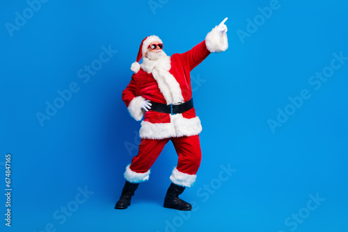 Full size photo of pensioner senior man point empty space dance dressed stylish santa claus costume coat isolated on blue color background