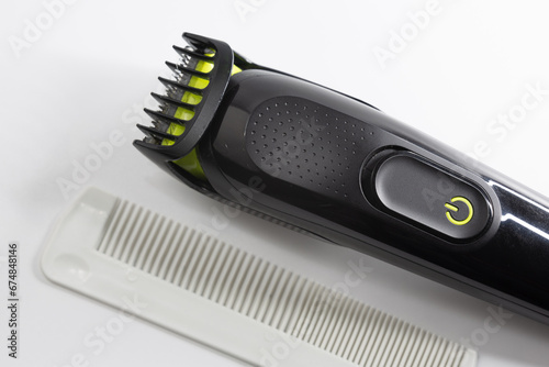 Electric shaver and plastic comb used for shaving hair, beard and moustache on a white background. Multi-purpose rechargeable shaver.
