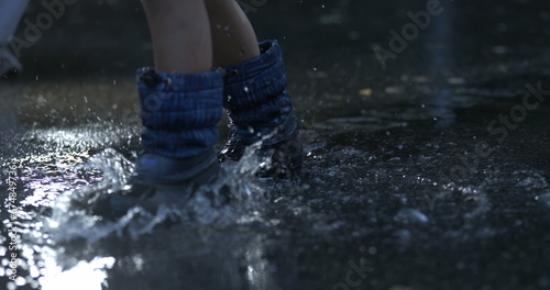 Child stepping in water puddle in super slow-motion wearing rainboots splashing liquid droplets everywhere captured with high-speed camera in 800 fps