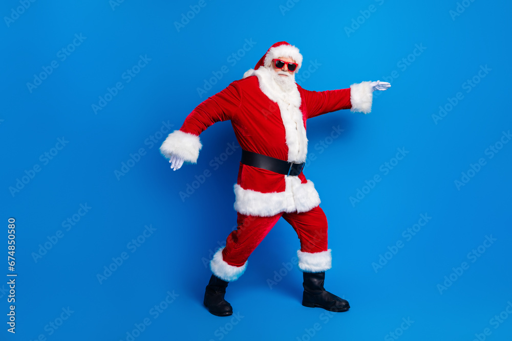 Full size photo of pensioner senior man sneak go deliver present dressed stylish santa claus costume coat isolated on blue color background Full size photo of pensioner senior man sneak go deliver present dressed stylish santa claus costume coat isolated on blue color background