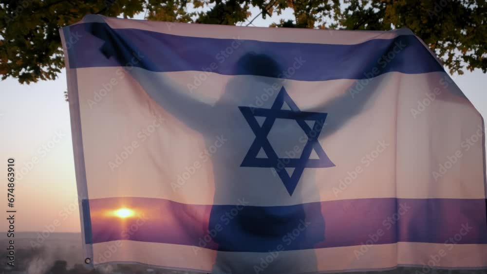 A woman stand with the flag of Israel against a clear sky at sunset.