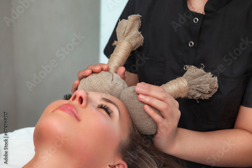 Beautician woman doing thai herbal massage skin face with bags to adult lady in beauty SPA, closeup. Medical cosmetics therapy massaging for patient. Health and anti aging concept. Copy ad text space