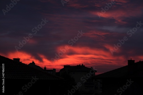 Amazing red sunrise sky with clouds over black silhouette of city buildings