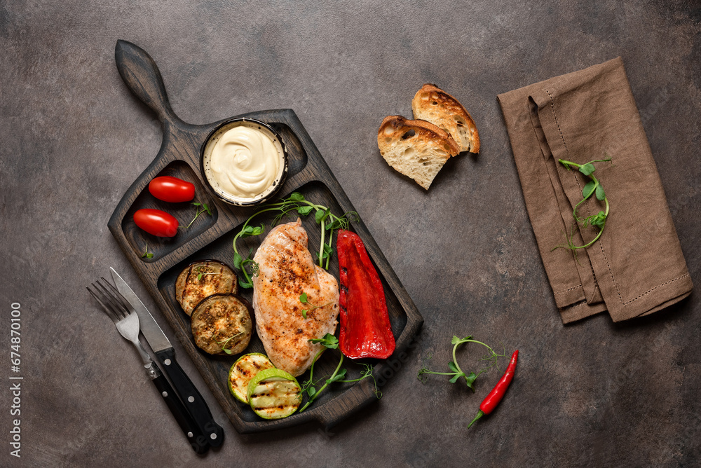 Grilled chicken fillet with grilled vegetables, sauce, toast . Dark rustic background. Top view, flat lay, copy space