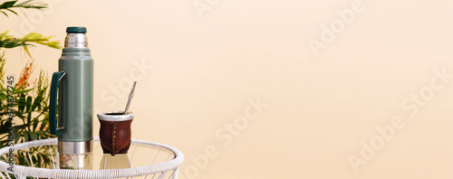Thermos and calabash mate cup with straw. In the backyard over a glass table. Yerba Mate, traditional South American hot drink. Wide banner format. photo